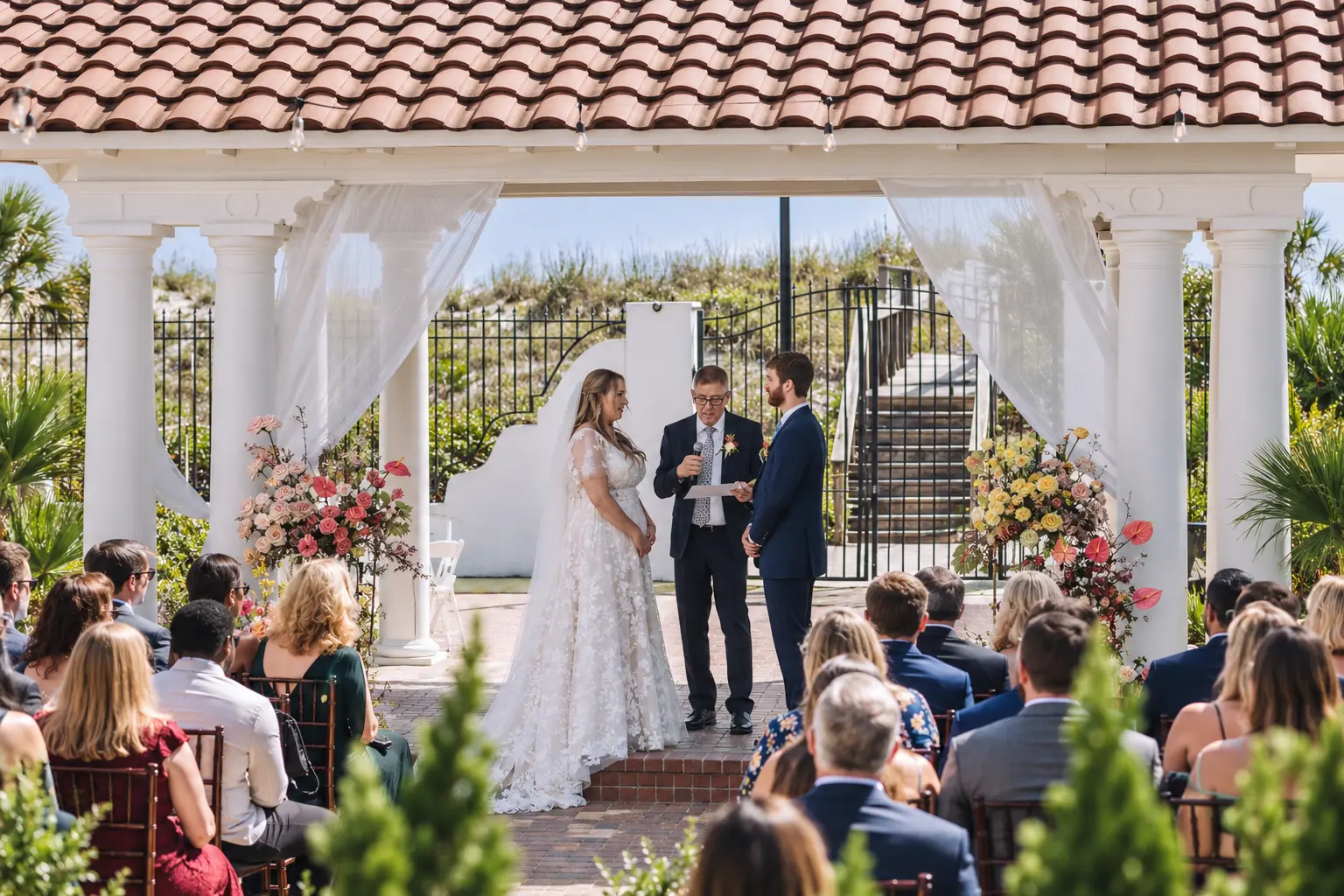 Bride, groom and officiant beneath a flower-lined pavilion